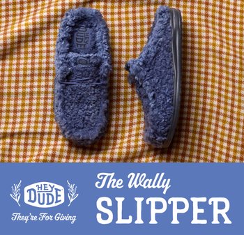 Pantofole blu pelose con suole di gomma posizionate su uno sfondo di tessuto a scacchi arancione e bianco.