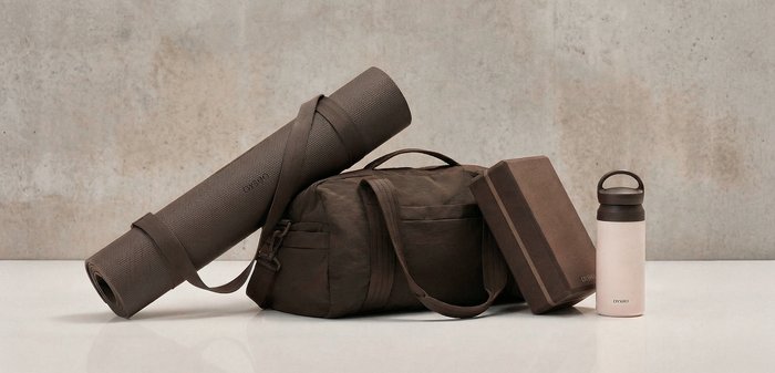 Brown yoga mat, matching gym bag, yoga block, and white water bottle with dark cap arranged on a white surface.