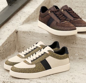 Dwie pary niskich sneakersów z materiałem w wzory i panelami z zamszu, jedna w kolorach beżowym i oliwkowym, druga brązowa, wystawione na schodach kamiennych.