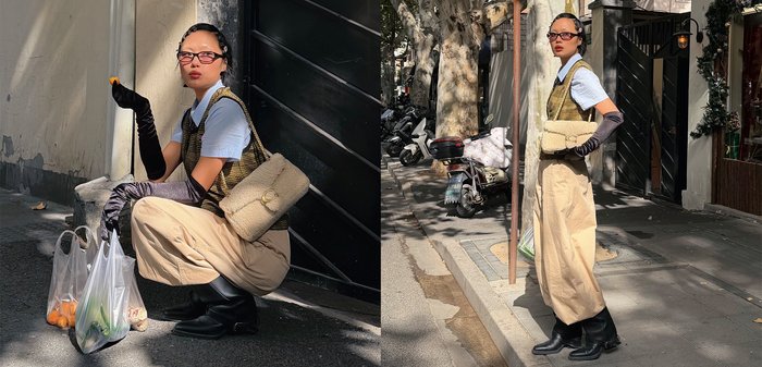 Frau in beigen Hosen, karierter Weste, weißem Hemd, schwarzen langen Handschuhen und Sonnenbrille, trägt eine cremefarbene Handtasche und hält Lebensmittel im Freien.