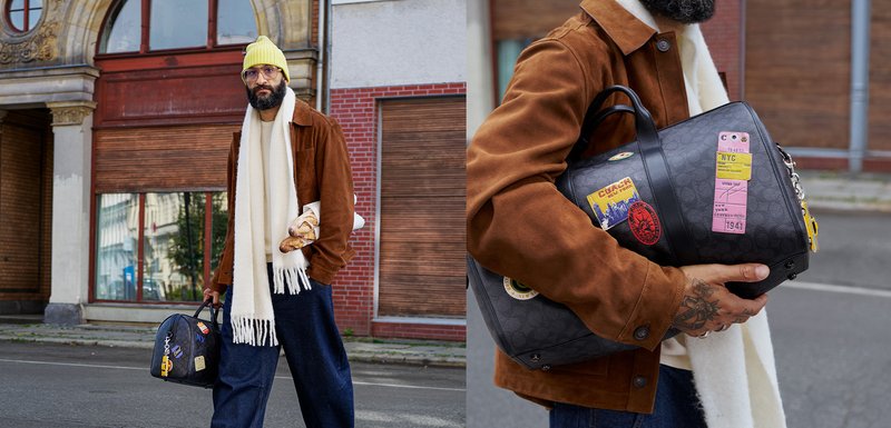 Sac en cuir noir avec plusieurs patchs et autocollants colorés, tenu par une personne portant une veste en daim marron et une écharpe blanche.