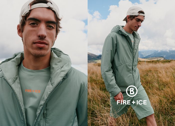 Junger Mann mit einer hellgrünen Jacke und weißer Kappe, der im Freien in einem bergigen Grasgebiet unter einem bewölkten Himmel steht.