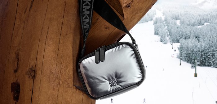 Silverfärgad vadderad crossbodyväska med svart rem med logotyp, två dragkedjor och slimmat, rundat rektangulärt utförande.