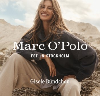 Uśmiechnięta kobieta z długimi włosami, ubrana w ciemną, oversize'ową bluzę i beżowe spodnie, siedzi na skalistym terenie pod pochmurnym niebem.