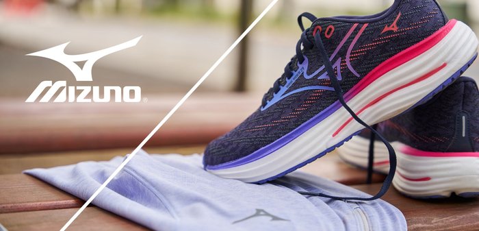 Zapatillas de running Mizuno con una parte superior de malla azul oscura y acentos en rosa y púrpura, acompañadas de una camiseta deportiva azul clara.