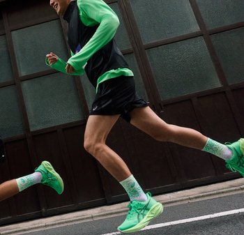 Twee hardlopers dragen felgroene hardloopschoenen en sokken en rennen op een straat met een achtergrond van donkere houten panelen.
