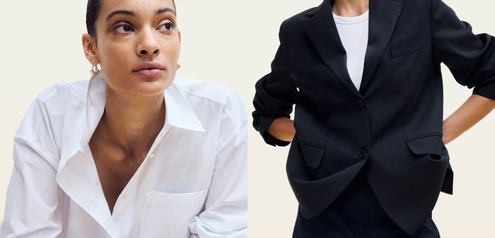 Personne portant un blazer noir aux manches retroussées sur une chemise blanche, mains posées sur les hanches, fond clair neutre.