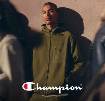 Giacca zip-up verde oliva con cappuccio e tasca frontale, caratterizzata da un logo discreto sul lato sinistro. Tessuto liscio e strutturato su uno sfondo chiaro.