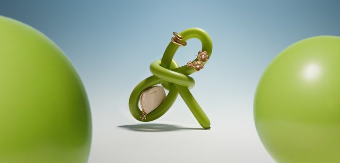 Zeleni balon, zvit v zanko, drži zlata prstana in majhen bež žepek na mehki modro-beli podlagi.