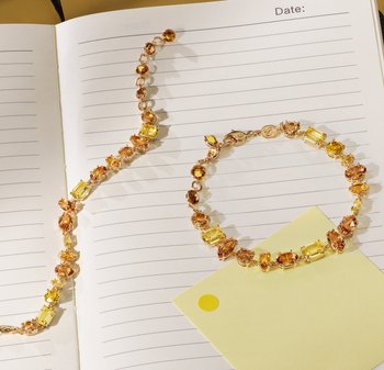 Zwei Armbänder auf linierten Papier präsentiert: eines in Gelb- und Bernsteintönen mit goldenen Akzenten, das verschiedene Edelsteinformen und -texturen aufweist.