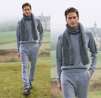 Grauer Strickpullover mit hohem Kragen und passender Hose, kombiniert mit einem strukturierten grauen Schal. Modell steht im Freien in einer grünen Landschaft.