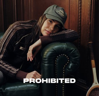 Brown knit sweater with ribbed cuffs, green cap with logo, resting on a dark green leather couch with brass studs. Text overlay: “PROHIBITED”.