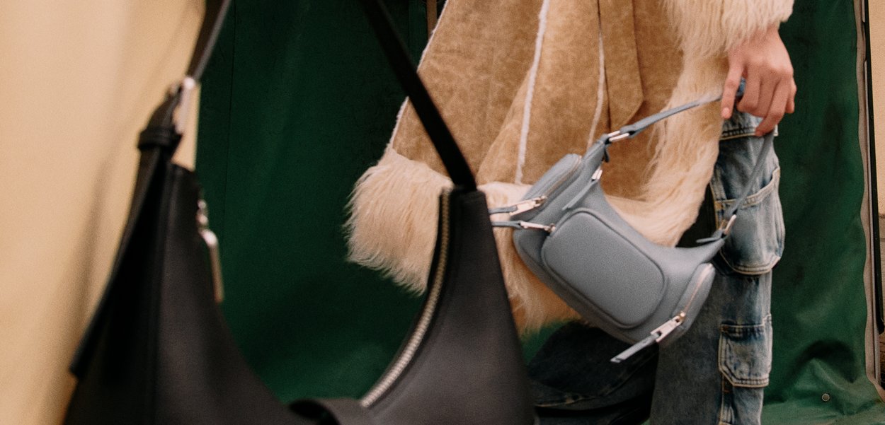 Jasnoniebieska torba o strukturalnym kształcie z krótkim paskiem, gładką fakturą, zamknięciem na zamek i nowoczesnym designem. W tle widoczna czarna torba.