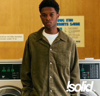 Braunes Cordhemd mit Reverskragen, Brusttasche und Knopfverschluss; über einem weißen T-Shirt getragen; steht neben einer Waschmaschine.