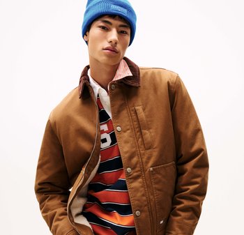 Brown canvas jacket with corduroy collar, featuring a zipper and side pocket, layered over a striped shirt, topped with a blue beanie.