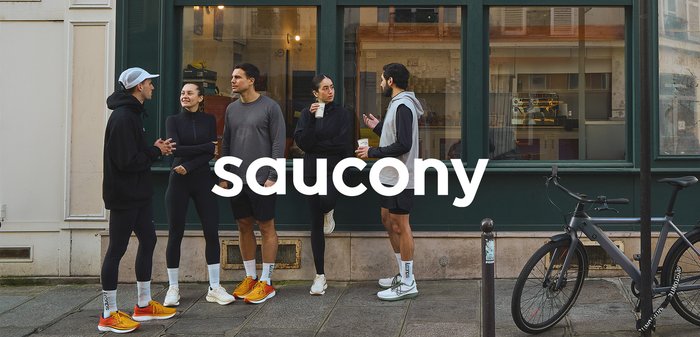 Group of five individuals in athletic wear, featuring black leggings, gray tops, and colorful sneakers. Background includes a green-framed window.