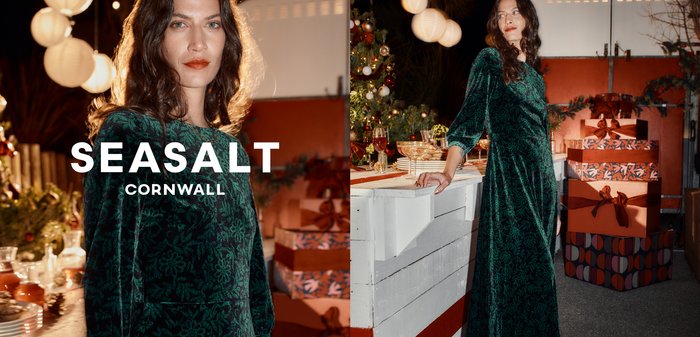 Zelené sametové šaty s květinovým vzorem, dlouhými rukávy a splývavou sukní. Pozadí je oživeno svátečním prostředím s dárky a výzdobou.