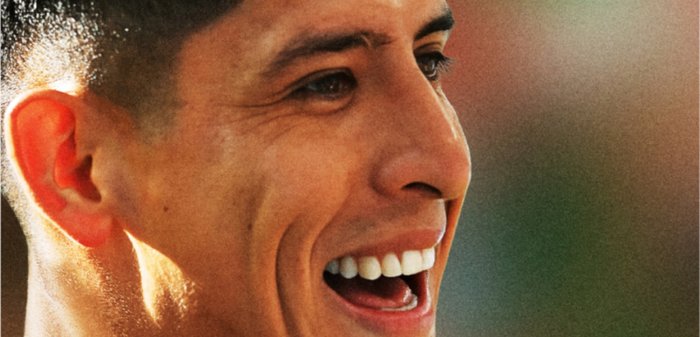 Zbliżenie na uśmiechniętego mężczyznę pokazującego zęby, z krótkimi ciemnymi włosami i widocznymi dołeczkami, patrzącego w prawo.