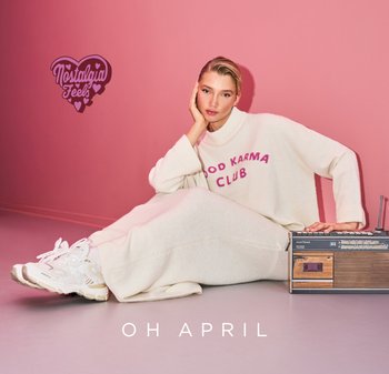 Cream-colored oversized sweater with "GOOD KARMA CLUB" in pink. White sneakers. Vintage radio with wooden accents. Pink background.