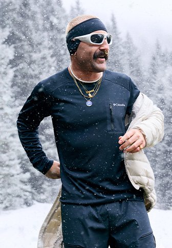 Μακρυμάνικη μαύρη μπλούζα που απορροφά την υγρασία με τσέπη στο στήθος, κάτω από ένα ανοιχτόχρωμο μπουφάν, συνδυασμένη με γυαλιά ηλίου και κορδέλα σε χιονισμένο τοπίο.