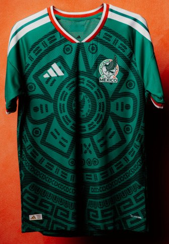 Maillot de football vert du Mexique avec motif du calendrier aztèque, logo Adidas blanc sur la poitrine droite et embleme du Mexique sur la poitrine gauche sur fond orange.