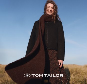 Brązowy dziergany szalik zarzucony na czarną kurtkę zapinaną na guziki oraz spódnicę w panterkę. W tle widoczne jest czyste niebieskie niebo i trawa.