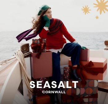 Červený svetr s vzorem, zelené rukavice a čepice. Tmavě modré kalhoty. Krabice v různých barvách s mašlemi. Pobřežní pozadí na lodi.