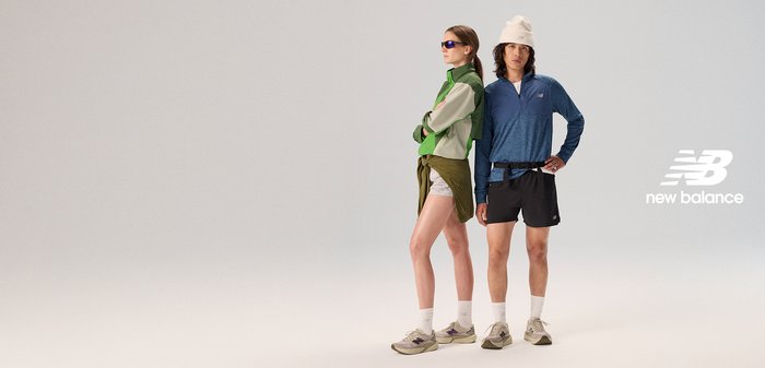 Athletic wear featuring a green and cream multi-layered jacket, blue long-sleeved top, black shorts, and neutral trainers.