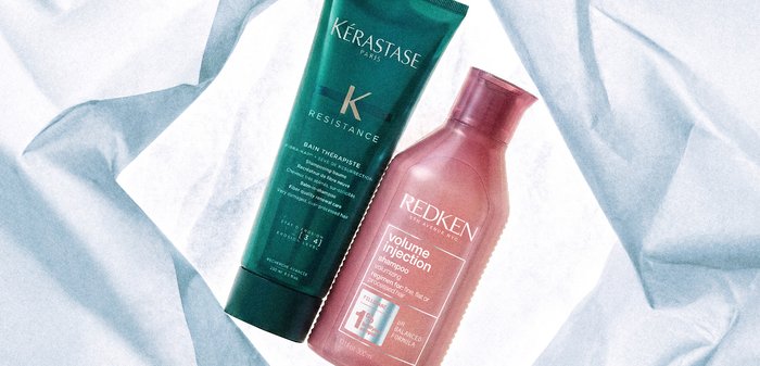 Tube de Kérastase Resistance Bain Therapiste et flacon de shampoing Redken Volume Injection sur fond de tissu blanc froissé.