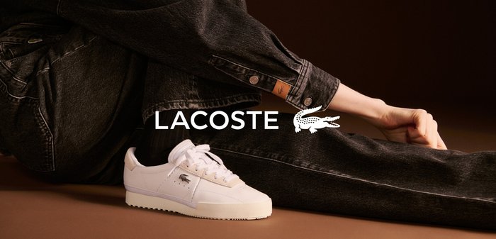 Białe trampki Lacoste ze gładkiej skóry, z perforacjami i płaskimi sznurówkami, w zestawieniu z ciemnoniebieskimi dżinsami z logo.