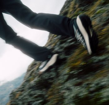 Schwarze Wanderschuhe mit weißen Akzenten und robusten Sohlen, die auf einem felsigen Gelände platziert sind und eine dynamische Gehbewegung zeigen.