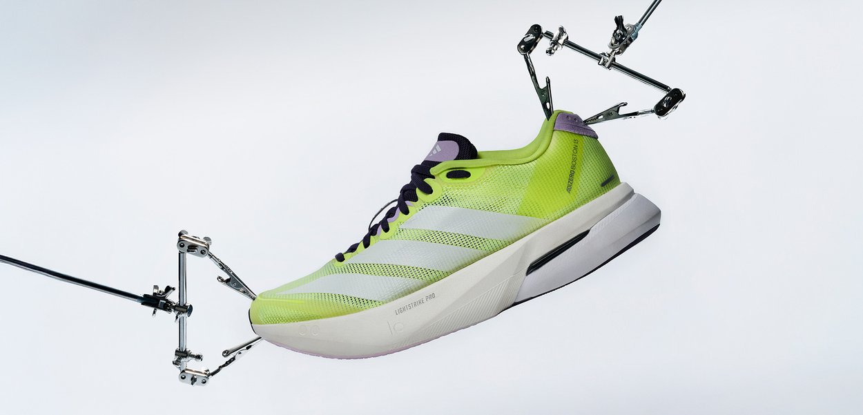 Pantof de alergare neon galben și alb ținut de cleme mecanice pe un fundal alb simplu.