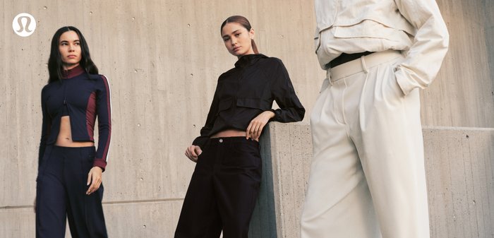 Three women wearing modern, fitted sportswear and wide-leg pants posing against a concrete wall under soft light.