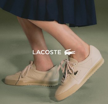 Sneaker beige con texture in pelle liscia, lacci piatti, suola in gomma e un piccolo logo ricamato di lato. Abbinato a una gonna blu navy.