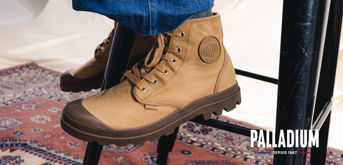 Bottes montantes en toile marron avec semelles épaisses en caoutchouc, portées avec un jean bleu, assises sur une chaise en métal noir sur un tapis à motifs.