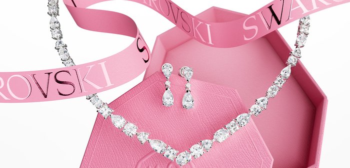 Collier en cristal ressemblant à un diamant et boucles d’oreilles pendantes assorties présentés avec une boîte Swarovski rose et un ruban sur fond blanc.