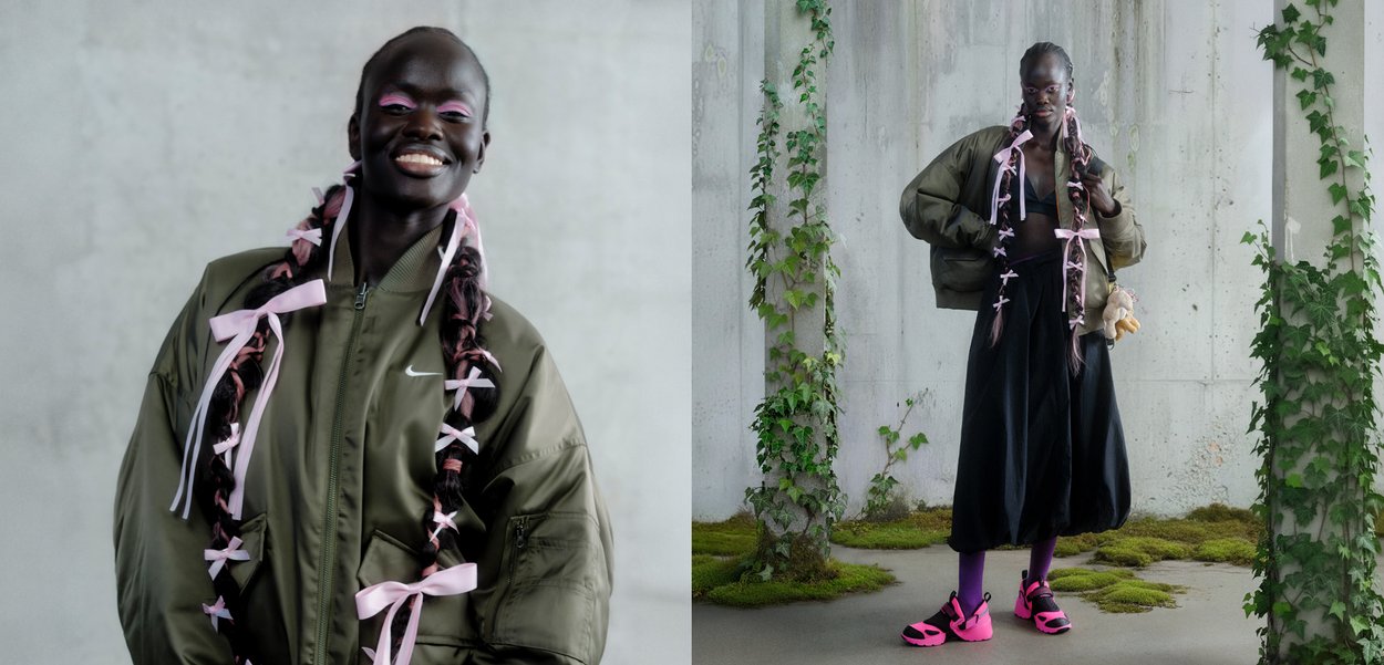 Jachetă bomber verde măsliniu, fustă neagră, cozi roz cu panglici, pantofi roz aprins, pe fundal de beton texturat cu verdeață.