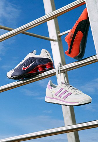 Tênis de corrida expostos em barras de metal: um modelo da Nike em azul-marinho e vermelho, um tênis laranja da Puma, e um Adidas cinza claro com listras roxas.