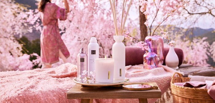 Witte kaars met een gestructureerd oppervlak, twee metalen spuitflessen, een witte vaas en een roze reflecterende vaas op een houten dienblad.