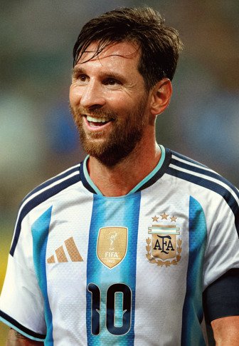 Joueur de football masculin souriant portant le maillot de l'Argentine numéro 10 avec un écusson FIFA, apparaissant sur un fond de stade flou.