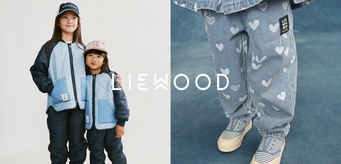 Two children in matching blue quilted jackets and pants, wearing caps, standing and embracing against a plain background.