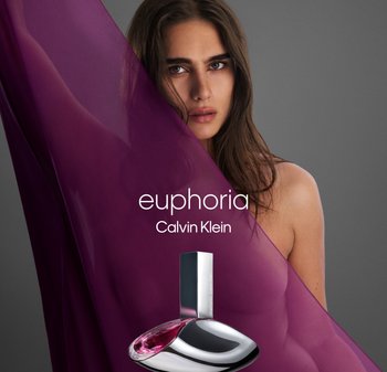 Profumo Calvin Klein Euphoria. Bottiglia in vetro viola scuro con design curvo e dettagli in argento. Tessuto viola traslucido sullo sfondo.