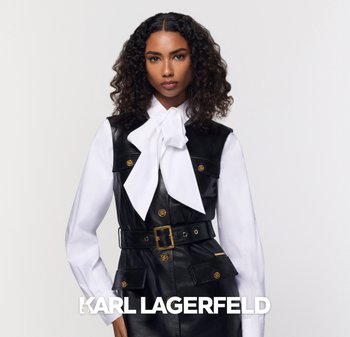 Black leather vest dress with gold hardware, large front pockets, and a belted waist, layered over a white blouse with a large bow neckline.