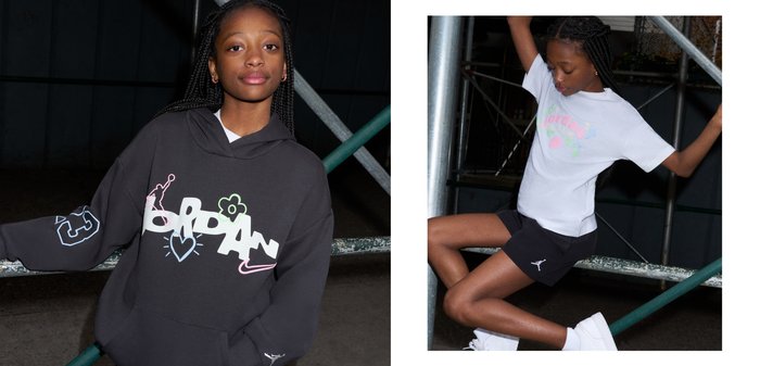 Jeune personne aux longs cheveux tressés portant un sweat à capuche sombre avec un logo "Jordan" coloré et des éléments graphiques, appuyée sur des barres métalliques la nuit.