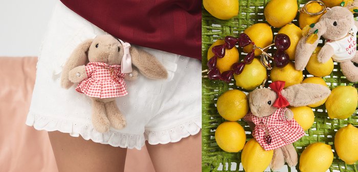 Hellgelbe Zitronen in einem grünen Korb mit zwei Plüsch-Hasen-Schlüsselanhängern, gekleidet in rot-weiße Outfits und mit roten Perlenaccessoires.
