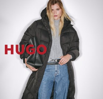 Schwarze Steppjacke mit Kapuze, strukturierten grauen Pullover, blaue Denim-Jeans und eine schwarze Handtasche. Bedeutende Merkmale sind ein Reißverschluss und das gepuffte Design.