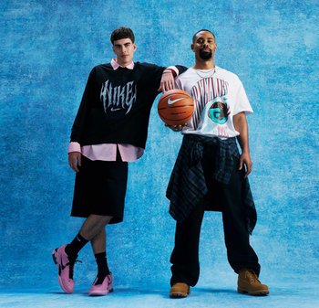 Due uomini in abbigliamento casual da strada posano contro uno sfondo blu, uno tiene in mano un pallone da basket e l'altro si appoggia alla sua spalla.