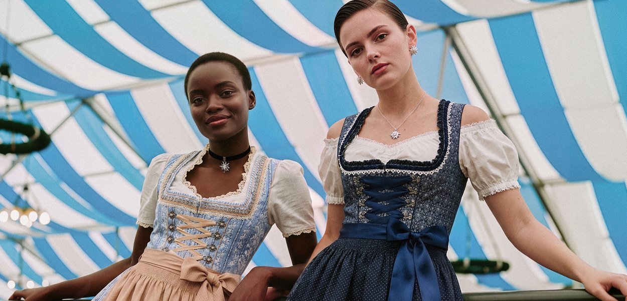 Deux femmes vêtues de robes traditionnelles bavaroises dirndl se tiennent sous un plafond de tente rayé bleu et blanc.