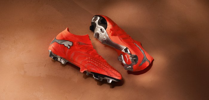 Chaussures de football synthétiques rouges avec une tige texturée, un logo PUMA bien visible, et une semelle argentée équipée de multiples crampons pour une meilleure traction.