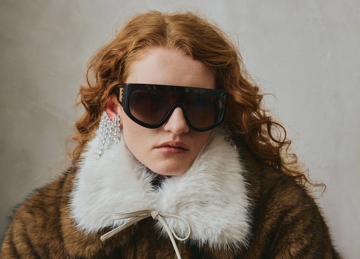 Μαύρα υπερμέγεθους γυαλιά ηλίου, χνουδωτός λευκός γιακάς, καφέ γούνινο παλτό και κρεμαστά σκουλαρίκια με κρύσταλλα δημιουργούν ένα τολμηρό, υφασμάτινο look.